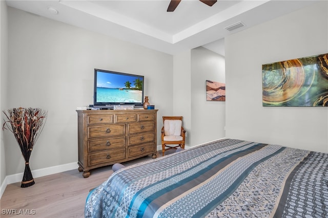 bedroom with ceiling fan, a tray ceiling, and light hardwood / wood-style floors