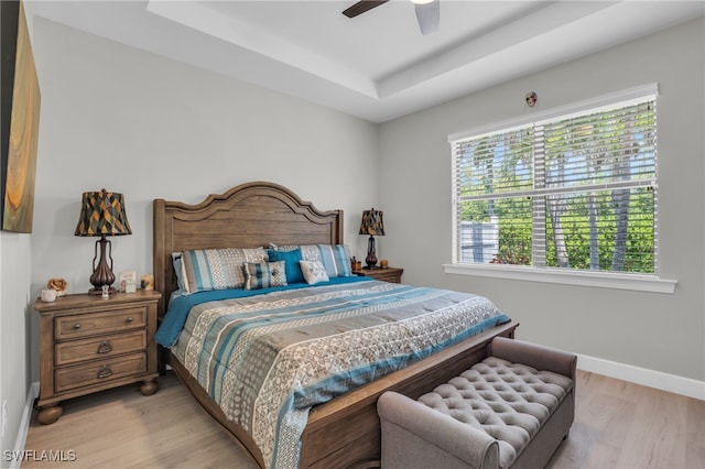 bedroom with ceiling fan, light hardwood / wood-style flooring, and a tray ceiling