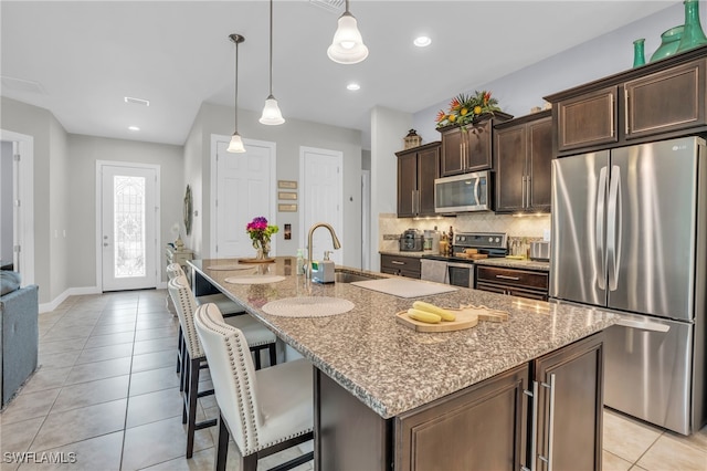 kitchen with stainless steel appliances, sink, light stone counters, a center island with sink, and pendant lighting