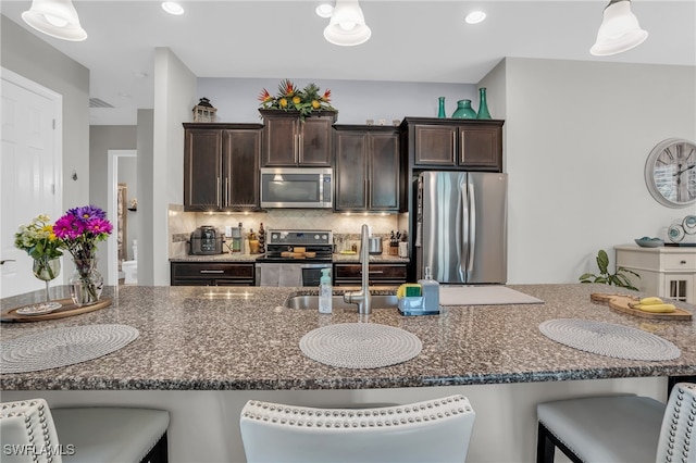 kitchen with decorative backsplash, a kitchen breakfast bar, hanging light fixtures, appliances with stainless steel finishes, and dark brown cabinets