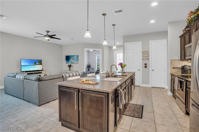 kitchen with ceiling fan, a kitchen island with sink, appliances with stainless steel finishes, light tile patterned floors, and dark brown cabinets