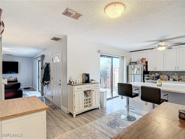 kitchen with ceiling fan, tasteful backsplash, stainless steel refrigerator, light hardwood / wood-style floors, and a textured ceiling