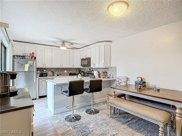 kitchen featuring stainless steel appliances, light hardwood / wood-style floors, white cabinets, and tasteful backsplash