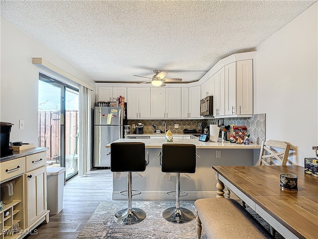 kitchen featuring appliances with stainless steel finishes, light hardwood / wood-style floors, decorative backsplash, ceiling fan, and a breakfast bar