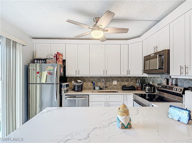 kitchen featuring sink, light stone countertops, ceiling fan, stainless steel appliances, and white cabinets