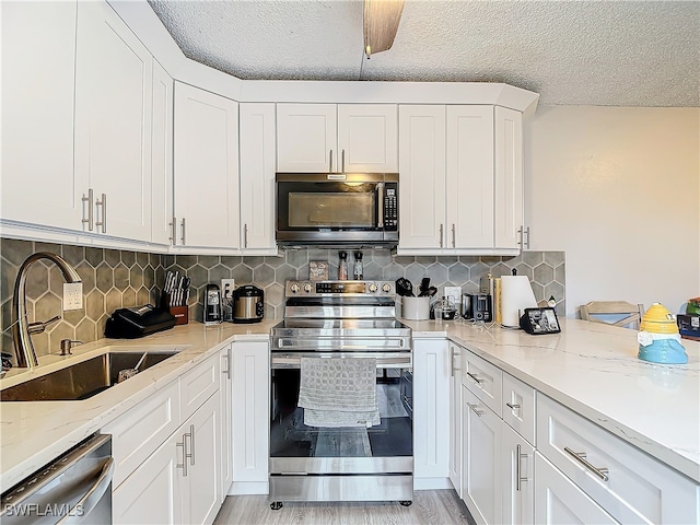 kitchen featuring sink, stainless steel appliances, white cabinetry, and light stone countertops