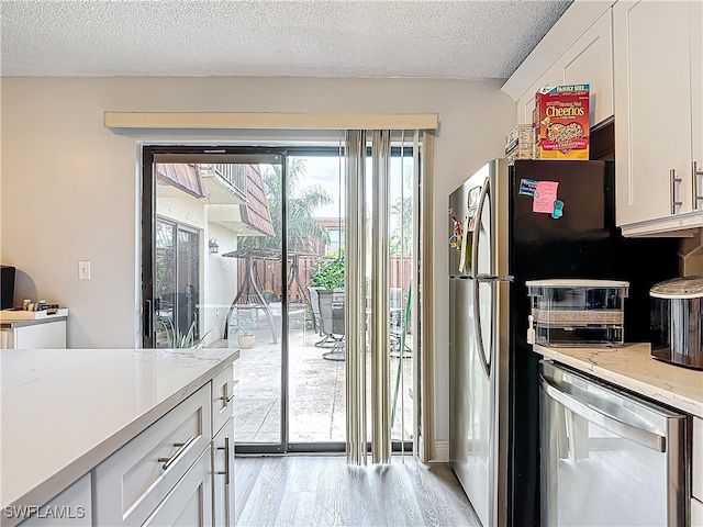 kitchen with appliances with stainless steel finishes, white cabinetry, a textured ceiling, and light wood-type flooring