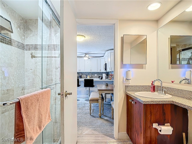 bathroom featuring ceiling fan, vanity, hardwood / wood-style floors, walk in shower, and a textured ceiling