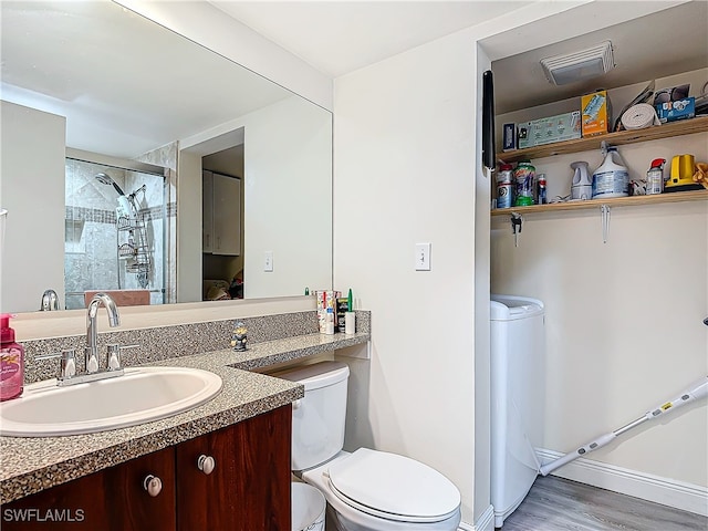 bathroom with hardwood / wood-style floors, toilet, a tile shower, and vanity