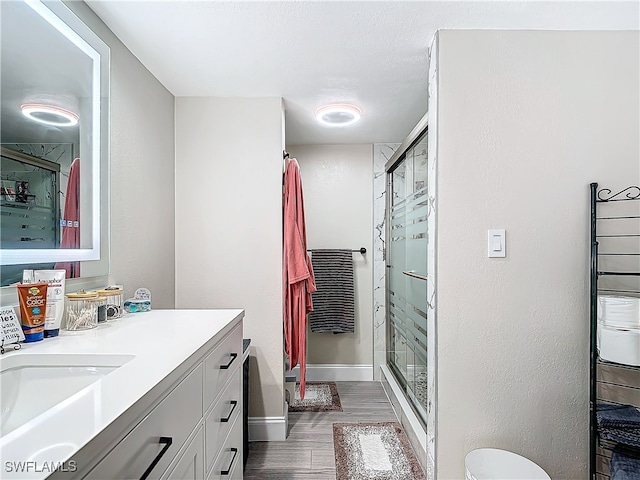 bathroom featuring wood-type flooring, toilet, vanity, and a shower with shower door