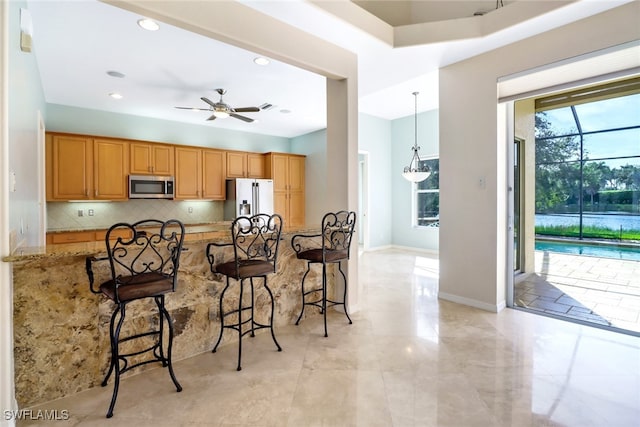 kitchen with a kitchen bar, ceiling fan, light stone countertops, and appliances with stainless steel finishes