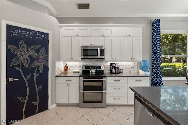 kitchen with appliances with stainless steel finishes, tasteful backsplash, light tile patterned floors, crown molding, and white cabinets