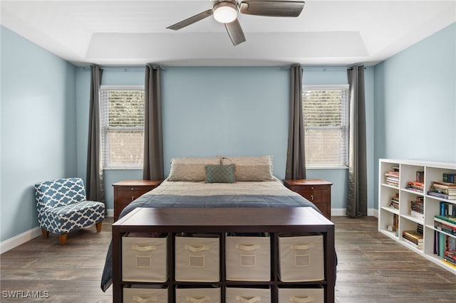 bedroom with dark hardwood / wood-style flooring, a tray ceiling, and ceiling fan