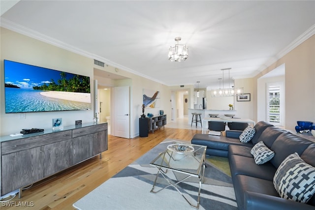 living area featuring crown molding, visible vents, a notable chandelier, and light wood-style flooring