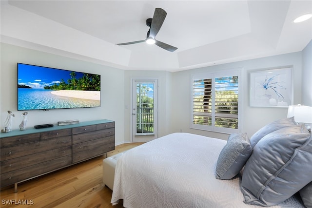 bedroom featuring light wood finished floors, access to outside, a tray ceiling, and ceiling fan