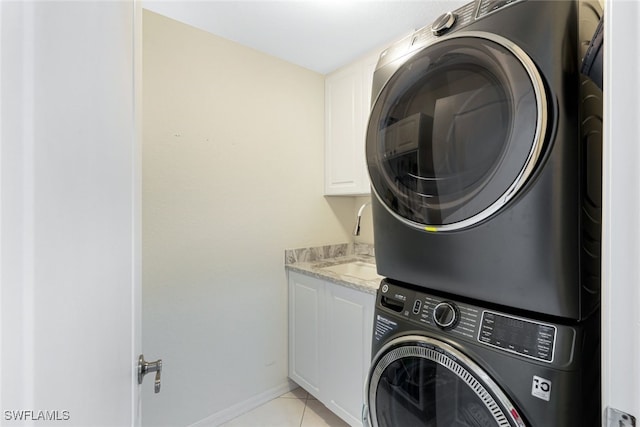 laundry room featuring light tile patterned floors, cabinet space, stacked washer / dryer, a sink, and baseboards