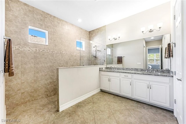 bathroom with double vanity, a sink, tile patterned flooring, baseboards, and walk in shower