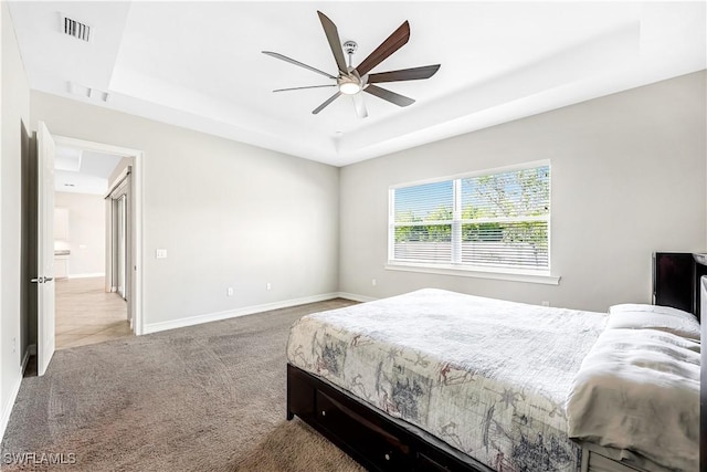 carpeted bedroom featuring a tray ceiling, a ceiling fan, visible vents, and baseboards