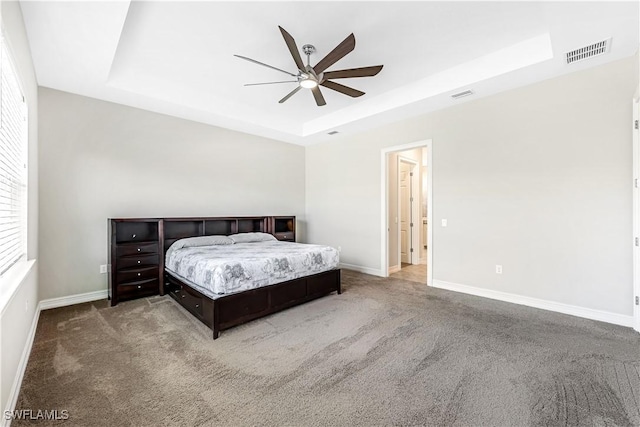 bedroom with a tray ceiling, carpet flooring, visible vents, and baseboards