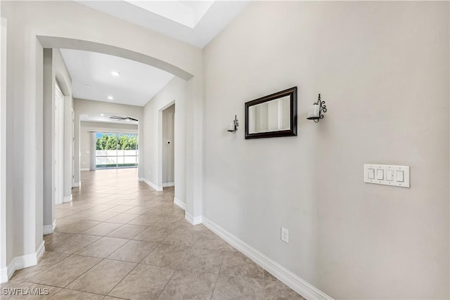 hall featuring light tile patterned floors, baseboards, arched walkways, and recessed lighting