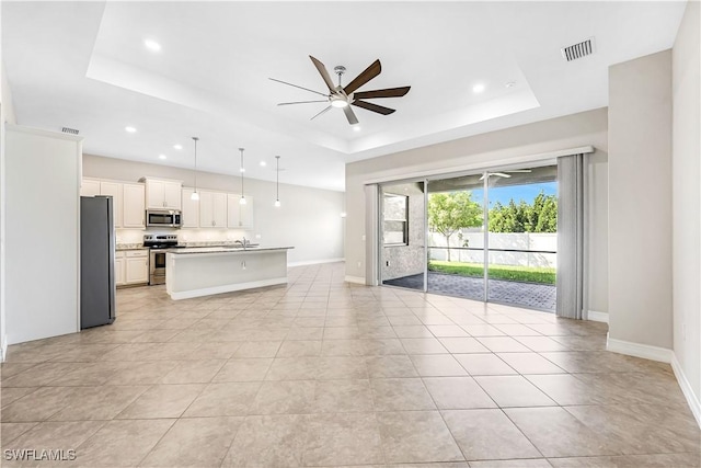 unfurnished living room featuring a raised ceiling, visible vents, ceiling fan, and baseboards