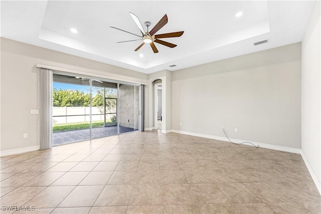 empty room featuring a tray ceiling, visible vents, arched walkways, and baseboards