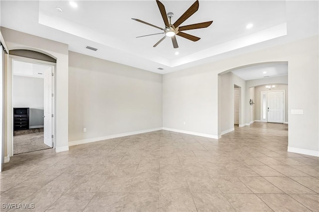 spare room featuring arched walkways, a tray ceiling, visible vents, and baseboards