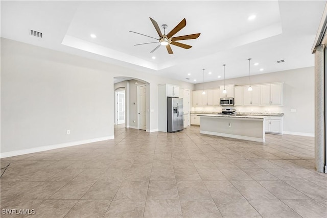 unfurnished living room with visible vents, a tray ceiling, arched walkways, and a ceiling fan