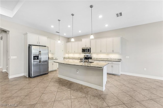 kitchen featuring stainless steel appliances, white cabinetry, a center island with sink, and light stone countertops