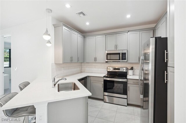 kitchen with kitchen peninsula, appliances with stainless steel finishes, a kitchen breakfast bar, hanging light fixtures, and gray cabinets