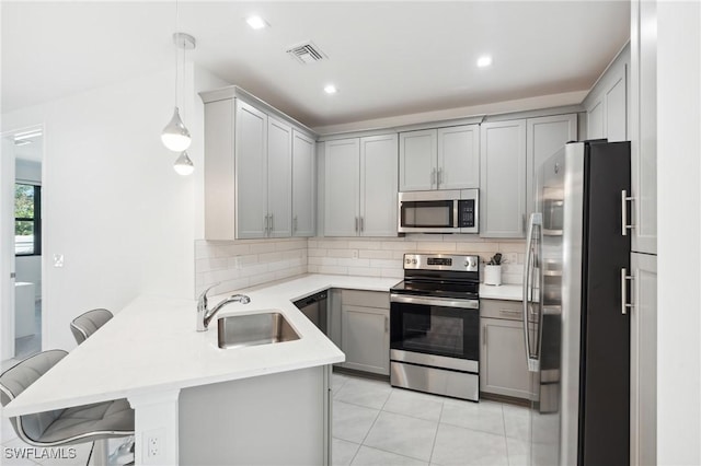 kitchen featuring stainless steel appliances, decorative light fixtures, gray cabinets, a kitchen bar, and kitchen peninsula