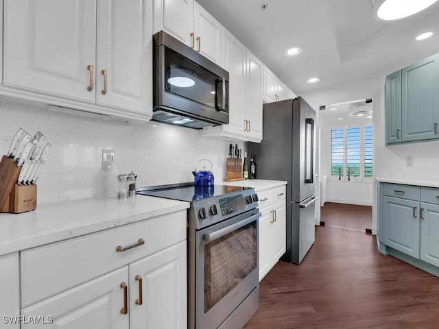 kitchen with appliances with stainless steel finishes, decorative backsplash, white cabinetry, light stone counters, and dark hardwood / wood-style flooring