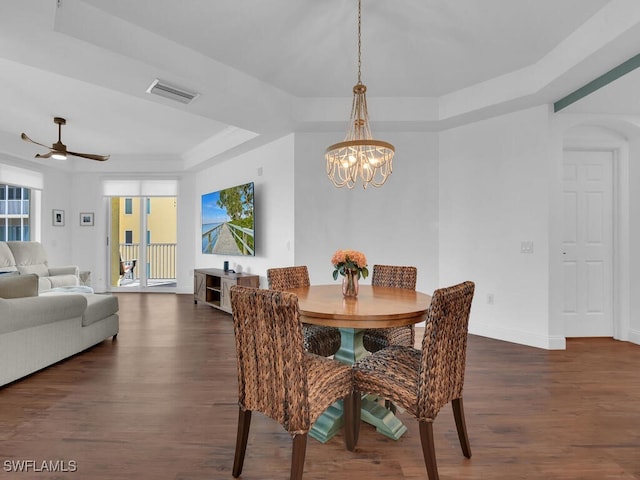 dining area featuring ceiling fan with notable chandelier, dark wood-type flooring, and a raised ceiling