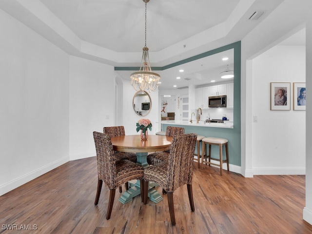 dining room featuring a notable chandelier, a tray ceiling, and wood-type flooring