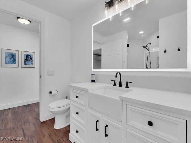 bathroom featuring a tile shower, toilet, vanity, and wood-type flooring