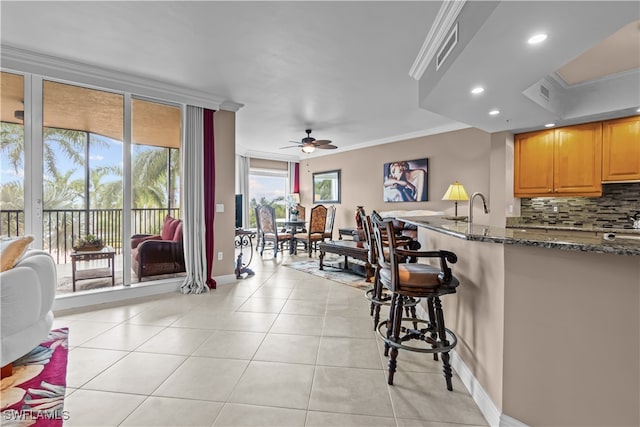 kitchen featuring dark stone countertops, ornamental molding, a kitchen bar, and decorative backsplash