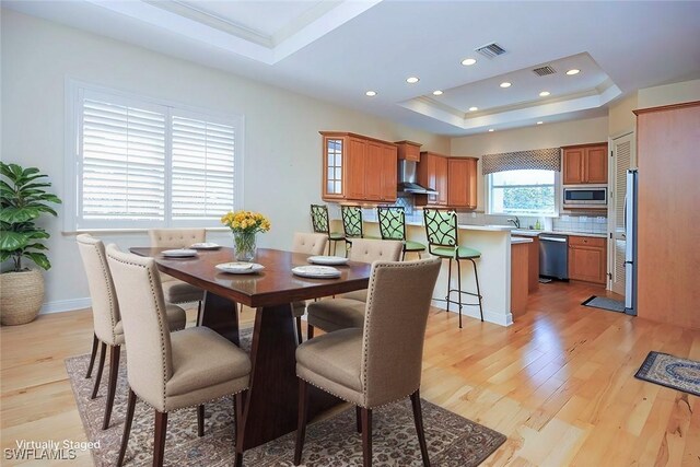 dining area with light hardwood / wood-style flooring and a raised ceiling