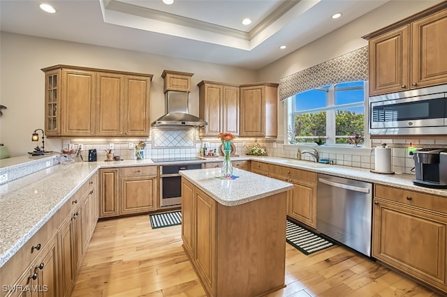 kitchen with a center island, light stone counters, stainless steel appliances, light hardwood / wood-style floors, and wall chimney range hood