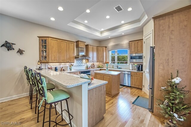 kitchen featuring a center island, light stone counters, stainless steel appliances, wall chimney exhaust hood, and tasteful backsplash