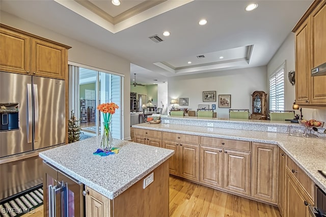 kitchen with light wood-type flooring, a tray ceiling, stainless steel refrigerator with ice dispenser, ceiling fan, and a kitchen island