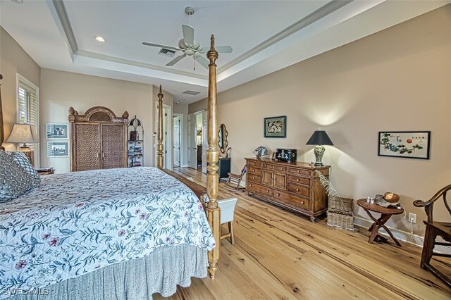 bedroom with light wood-type flooring, a tray ceiling, and ceiling fan