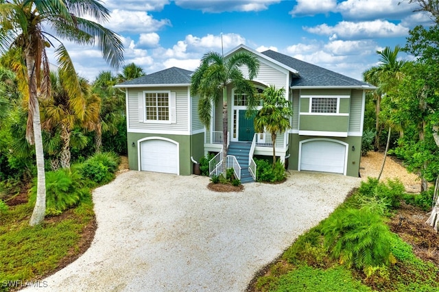 view of front of home with stairway, an attached garage, and gravel driveway