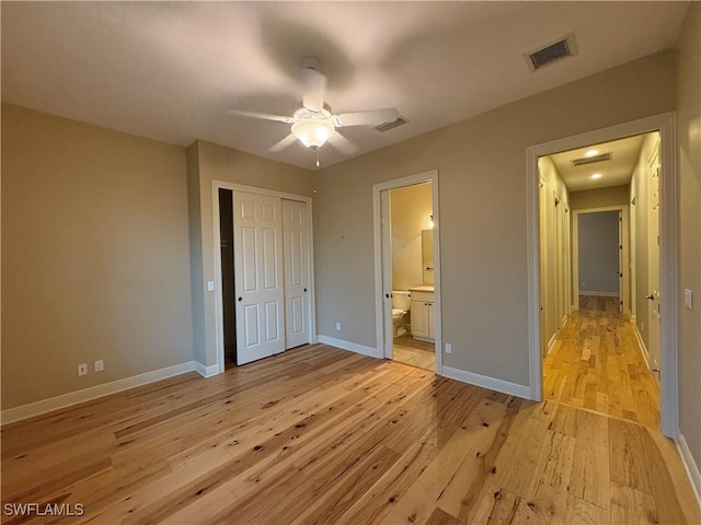 unfurnished bedroom with light wood-style flooring, visible vents, baseboards, a closet, and ensuite bath