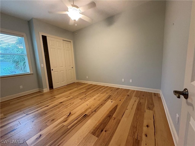 unfurnished bedroom featuring a ceiling fan, a closet, light wood-style flooring, and baseboards