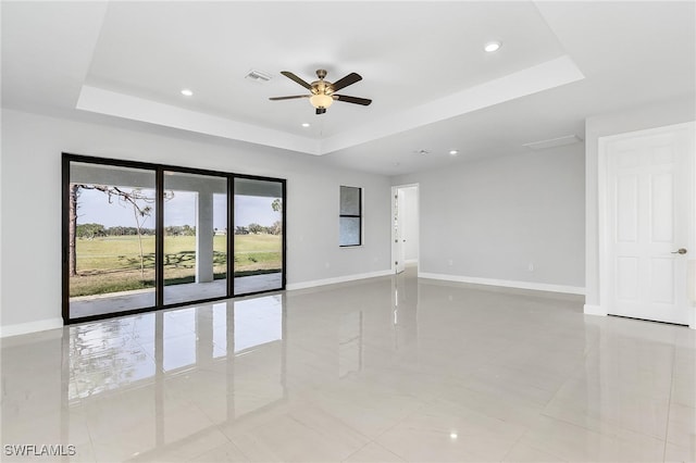 tiled empty room featuring ceiling fan and a raised ceiling