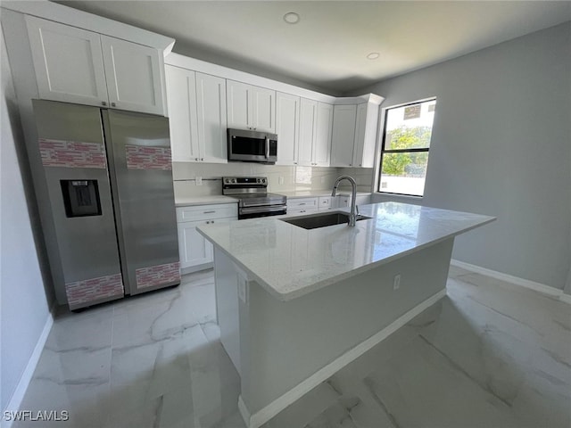 kitchen with a center island with sink, stainless steel appliances, sink, white cabinetry, and light stone counters