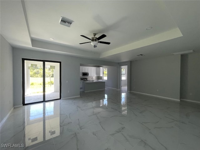 unfurnished living room with a tray ceiling, sink, and ceiling fan