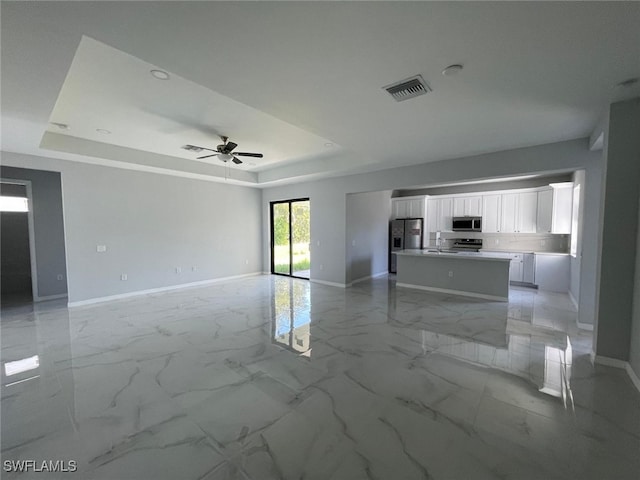 unfurnished living room featuring ceiling fan, sink, and a tray ceiling