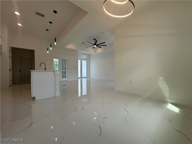 unfurnished living room featuring sink, ceiling fan, and a raised ceiling