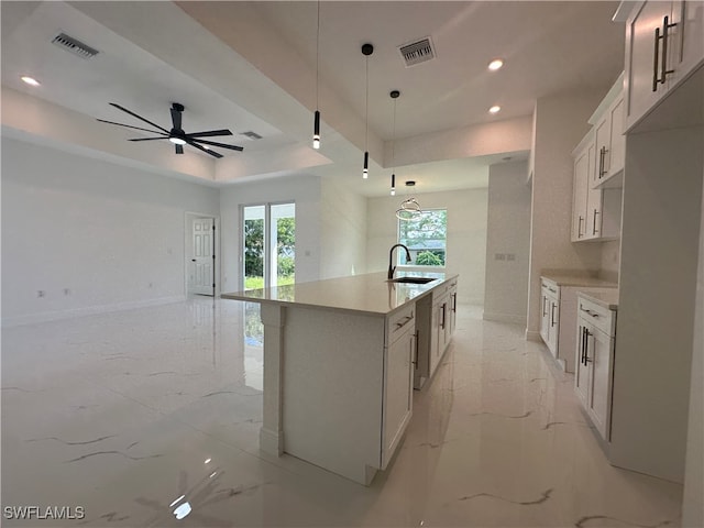 kitchen with white cabinets, hanging light fixtures, a center island with sink, ceiling fan, and sink